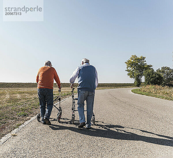 Active senior friends walking on road holding mobility walker