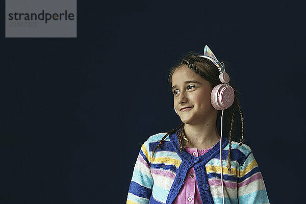 Smiling girl listening music through headphones in front of blue background