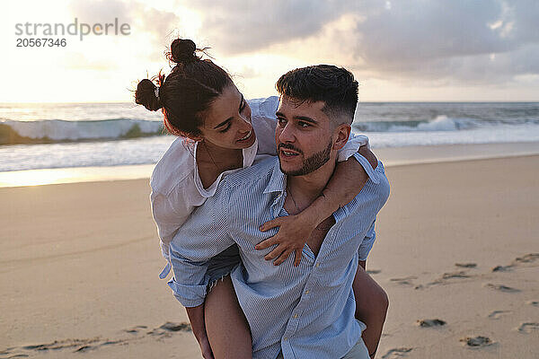 Man carrying girlfriend on beach at sunset