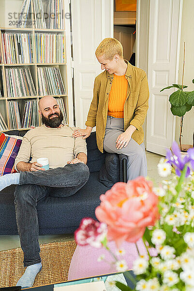 Smiling woman with hand on shoulder of man sitting on sofa at home