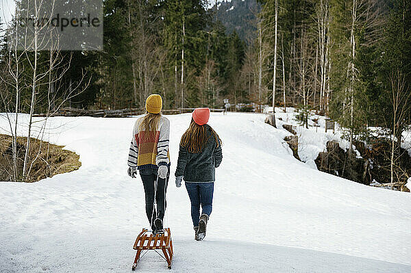 Woman pulling sled walking with friend on snow field