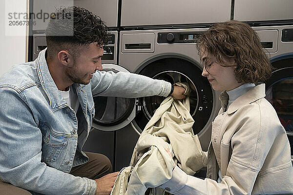 Smiling couple removing sheet from washing machine in laundromat