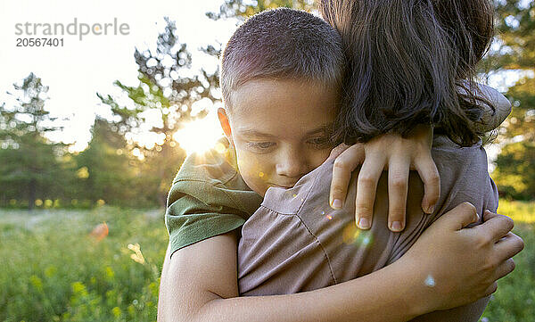 A boy hugs his mother in the park.