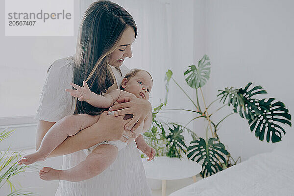 Smiling mother playing with baby boy near plants at home