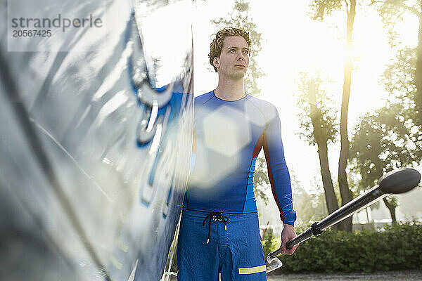 Handsome young man carrying paddleboard and oar