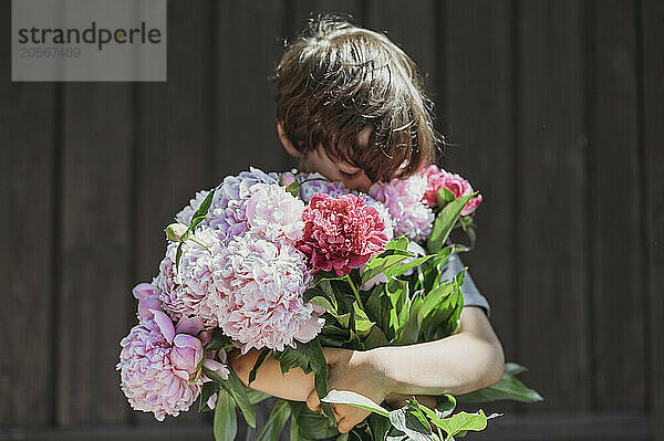 Cute boy with bouquet of peonies at back yard