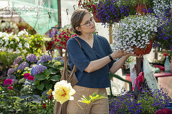 Short hair woman choosing flowering plant in garden center