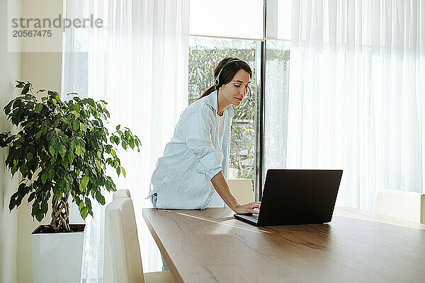 Confident customer service representative with headset using laptop on table working at home