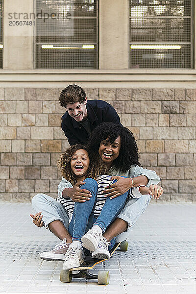 Father pushing mother and daughter sitting on skateboard