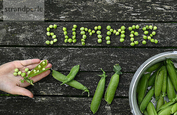 Hand of girl with spelling of summer made from fresh green peas over wooden table