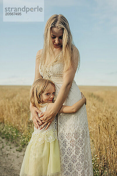 Cute girl embracing sister and standing on wheat field during summer