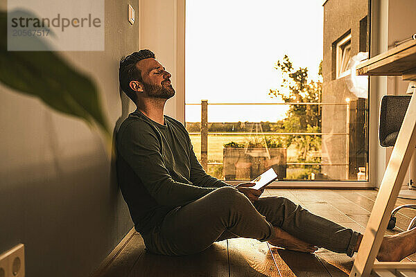 Man with eyes closed and tablet PC sitting on floor