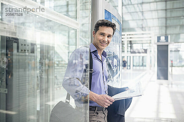 Smiling businessman with shoulder bag and document at airport