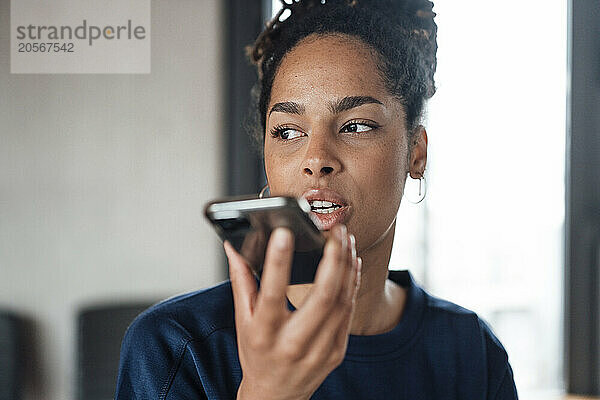 Confident young businesswoman talking through mobile phone speaker at office