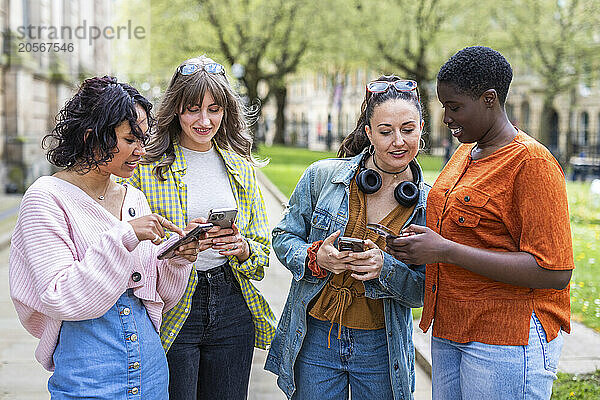 Multiracial female friends using smart phones standing together