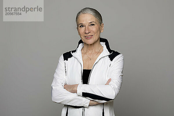 Smiling senior woman standing with arms crossed against gray background