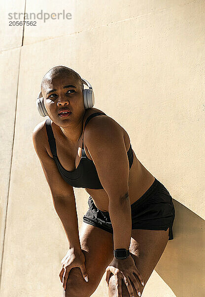 Exhausted sporty woman with hand on knees leaning on wall