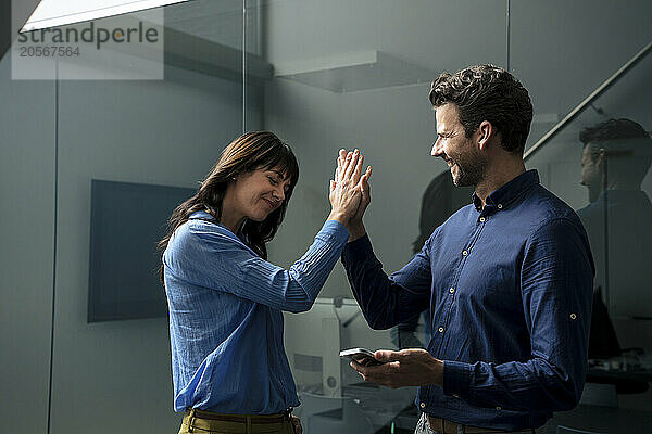 Happy businessman holding smart phone and giving high-five to businesswoman in home office