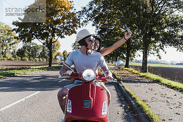 Happy young couple taking selfie on motor scooter at country road