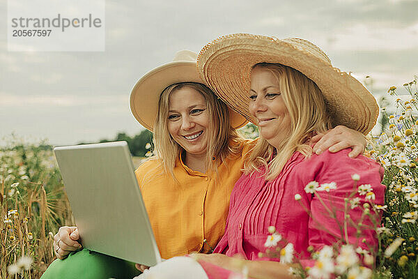 Happy women using laptop at chamomile field