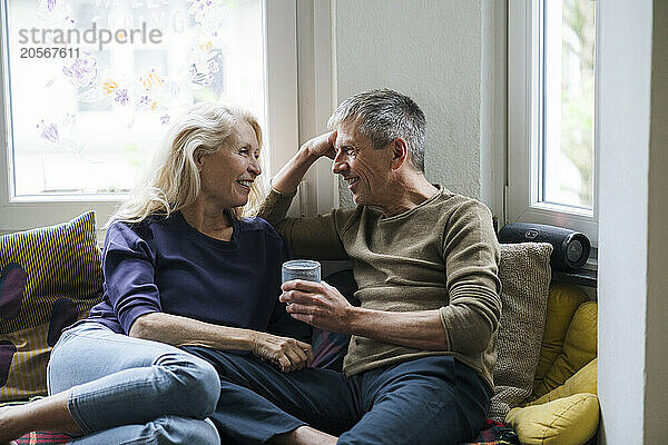 Smiling retired couple sitting on alcove window seat at home