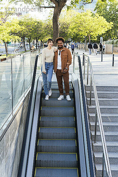 Happy couple standing on escalator moving down in subway