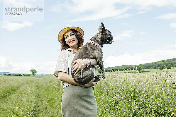 Happy woman standing with french bulldog on sunny day in field