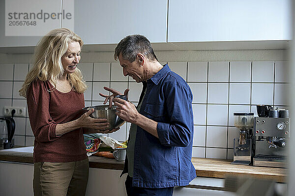 Retired senior couple with mixing bowl standing in kitchen at home