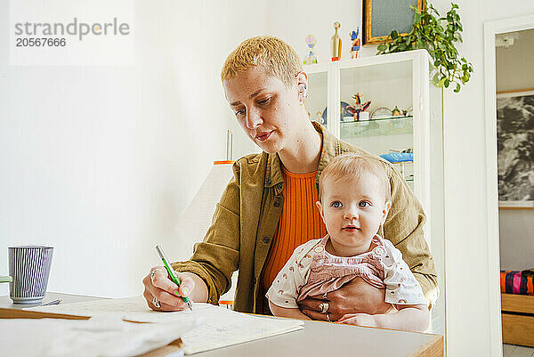 Woman writing in diary and sitting with toddler daughter at home