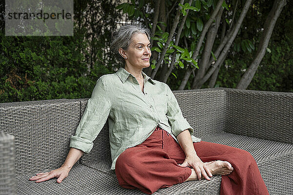 Thoughtful mature woman sitting on sofa at terrace