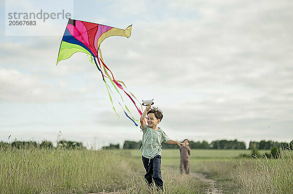 Happy boy running with kite and brother in background