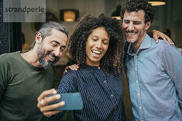 Business professionals holding smartphone and taking selfie near cafe