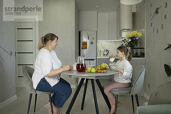 Mother and daughter having breakfast sitting at dining table in home