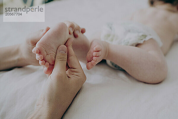 Hands of mother massaging baby's foot at home