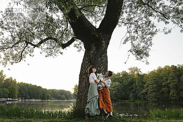 Girl with mother and dog in front of tree near river at park