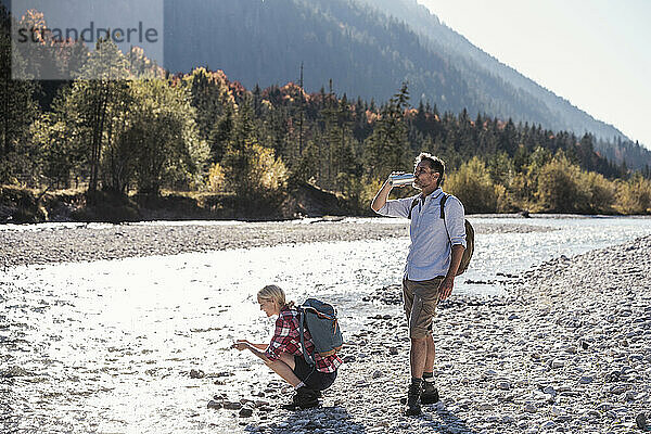 Mature man drinking water by friend near river