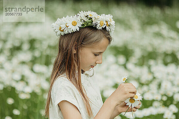 Girl wearing fresh daisy flower wreath in field