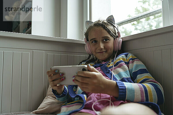 Smiling girl wearing headphones using mobile phone on sofa at home