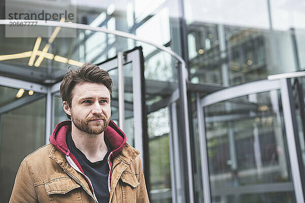 Contemplative man in brown jacket near public building