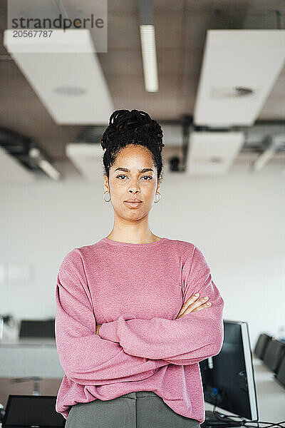 Confident young businesswoman standing with arms crossed standing at workplace