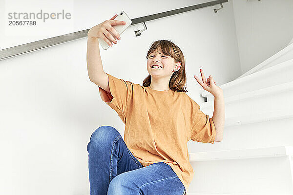 Happy girl taking selfie through smart phone sitting on staircase at home