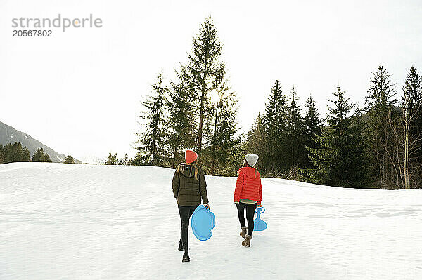 Friends carrying sleds walking on snow field