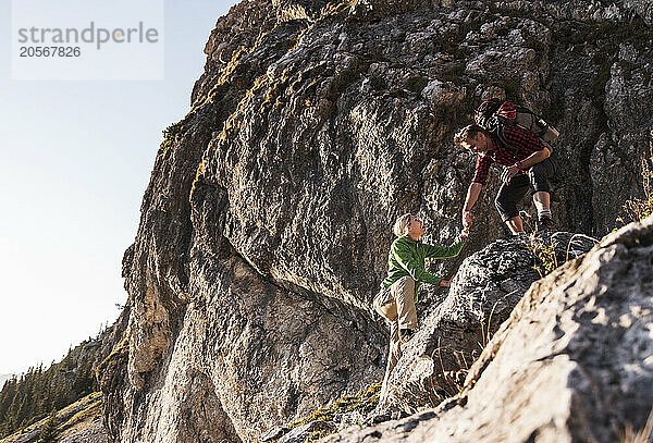 Happy man helping girlfriend climb mountain in Tyrol