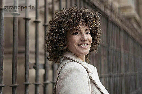 Smiling woman with curly hair near metal fence