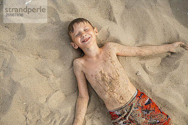 Boy with eyes closed lying down on sand at beach