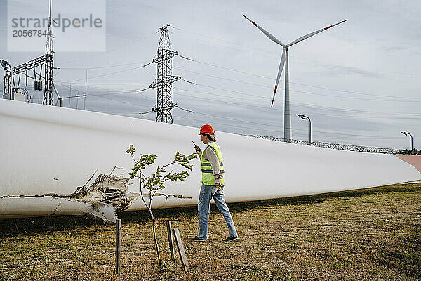 Engineer inspecting damaged blade of wind turbine at field