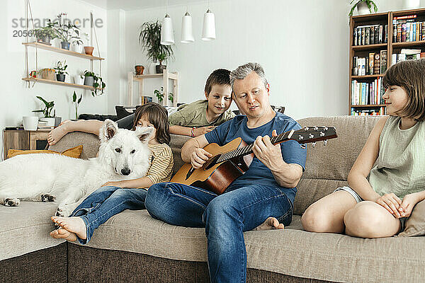 Father playing guitar with children at home