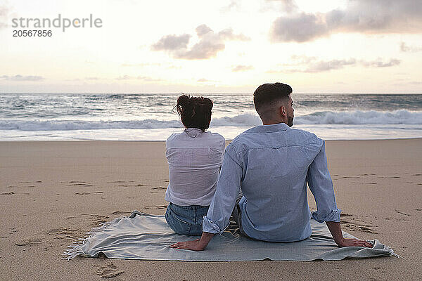 Boyfriend and girlfriend sitting on blanket looking at sea