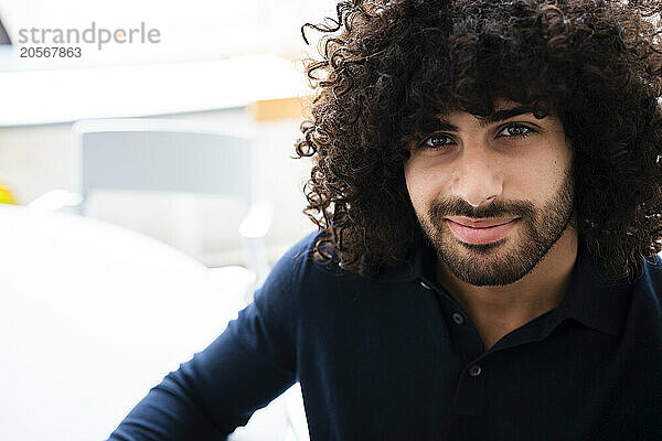 Smiling handsome young businessman with curly hair and stubble at workplace