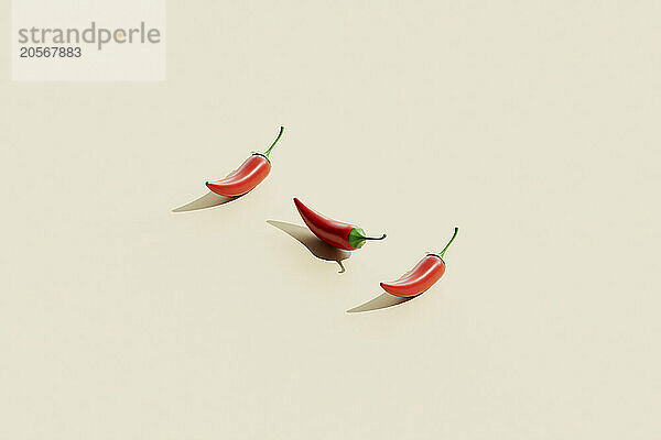 Three red chili peppers arranged on beige background